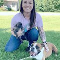 A woman sitting with three dogs and smiling at the camera.